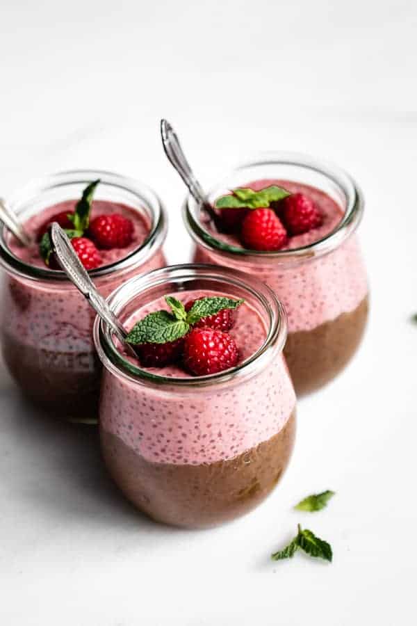 three cups of chocolate and raspberry chia pudding topped with raspberries and fresh mint