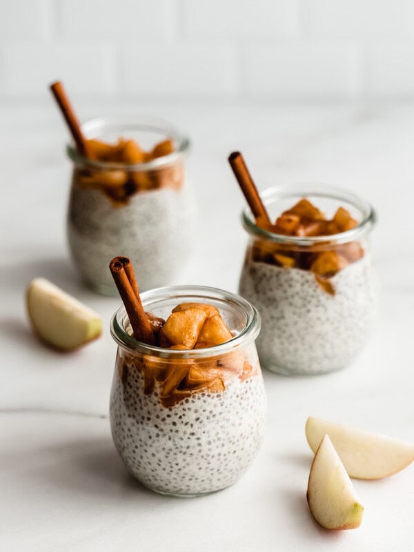three jars of chia pudding topped with cinnamon apples on a marble countertop