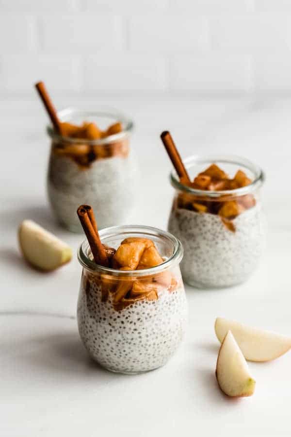 three jars of chia pudding topped with cinnamon apples on a marble countertop