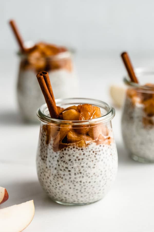 a jar of chia pudding topped with cinnamon apples and a cinnamon stick in it