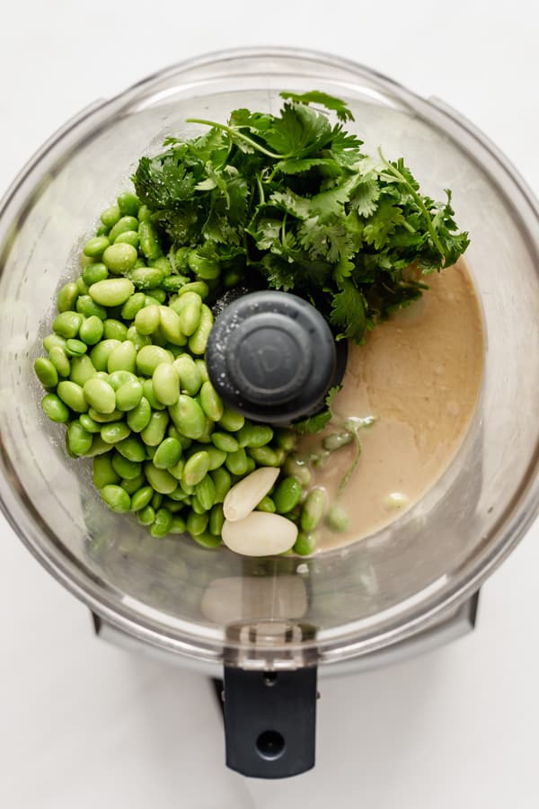 A food processor with edamame, cilantro, tahini and garlic in it