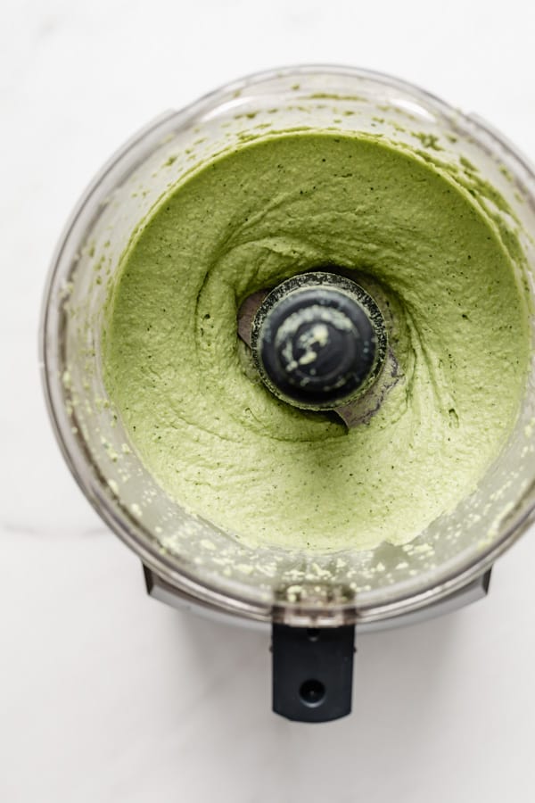 a food processor with green edamame hummus in it