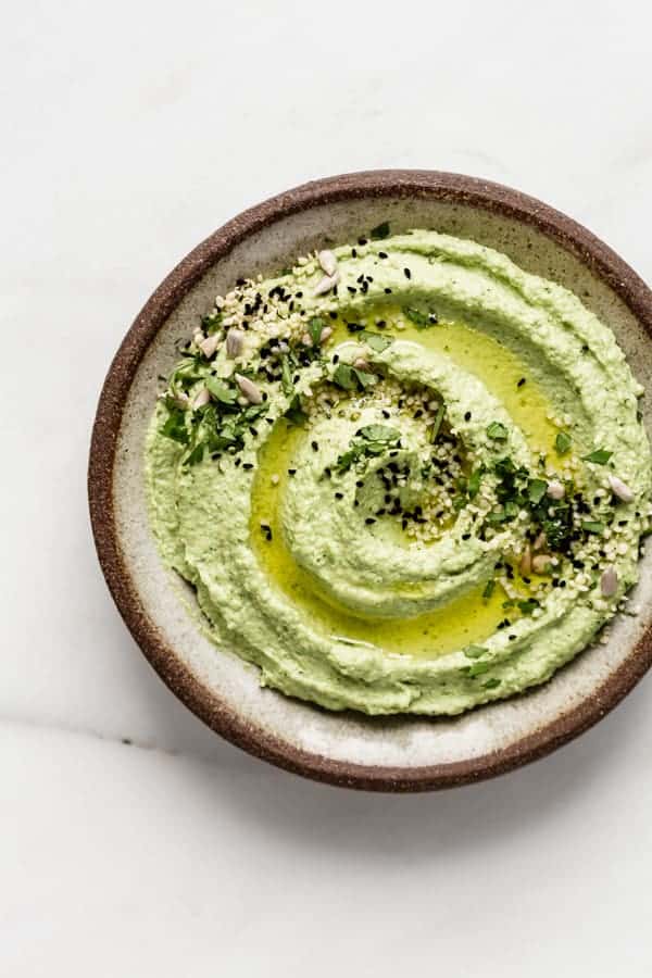 edamame hummus topped with olive oil, seeds and chopped cilantro on a brown ceramic plate
