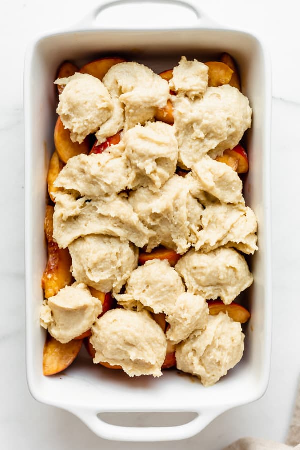 an unbaked peach cobbler in a white baking dish