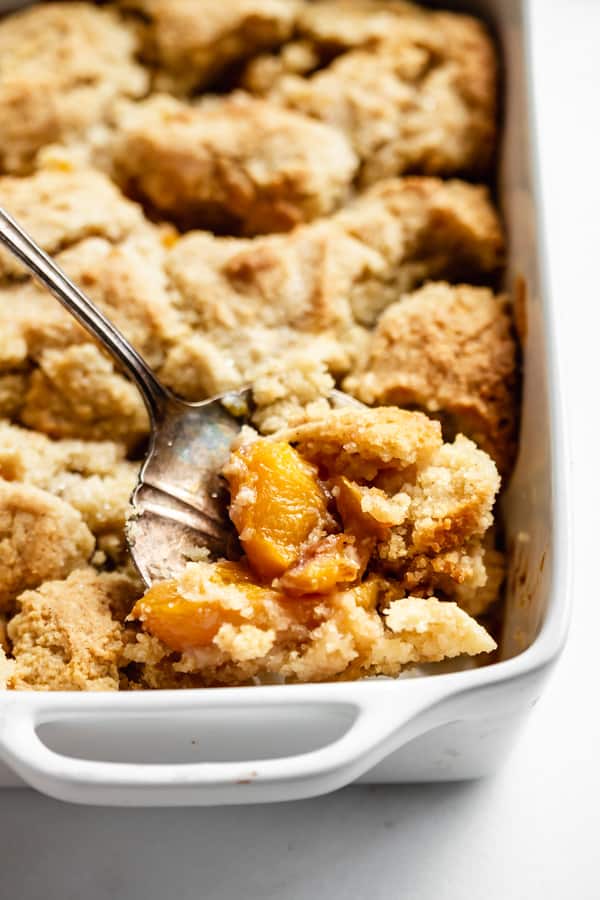 a piece of gluten-free peach cobbler being scooped out of a baking dish with a serving spoon
