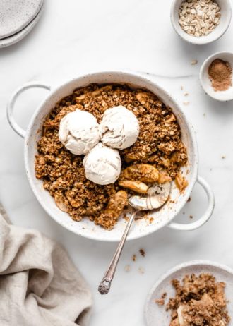 apple crisp in a baking dish topped with three scoops of vanilla ice cream