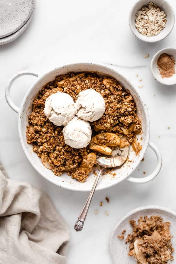 an apple crisp in a round baking dish with three scoops of vanilla ince cream on top