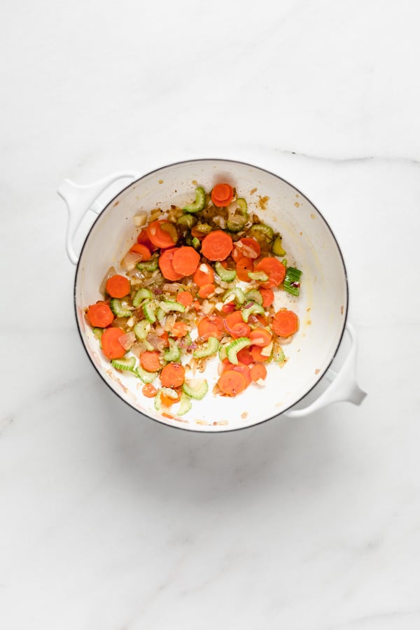 A white pot with chopped u carrots celery and shallots in it