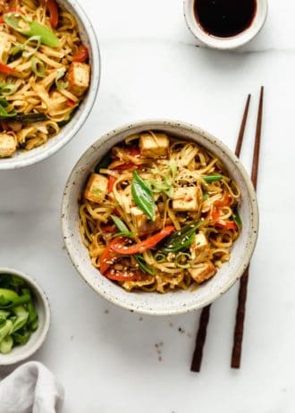 Singapore noodles in a speckeld ceramic bowl with wooden chopsticks on the sie
