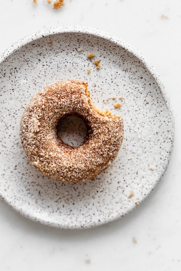a vegan apple cider donut with a bite taken out of it on a white speckled plate