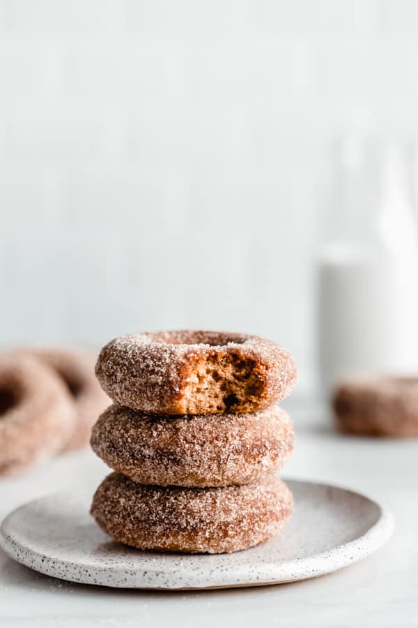 A stack of three apple cider donuts on a white speckled plate 