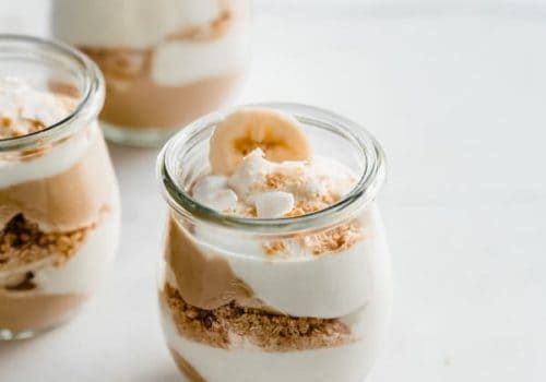 a cup of banana cream pie parfait with layers of pudding, coconut whipped cream, graham cracker crumbs and banana
