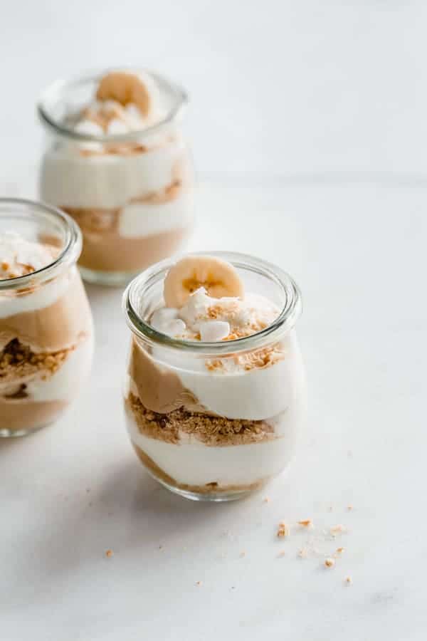 a cup of banana cream pie parfait with layers of pudding, coconut whipped cream, graham cracker crumbs and banana