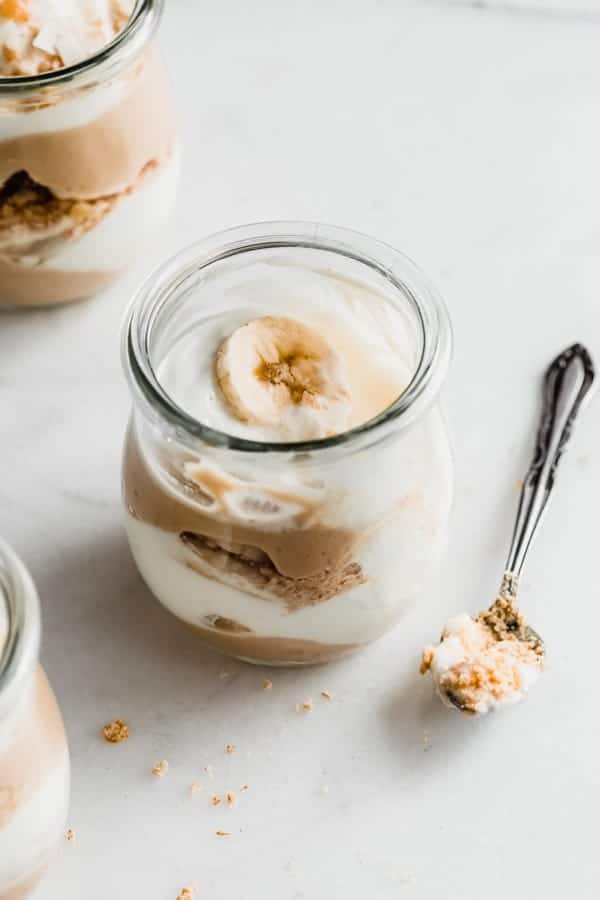 a cup of vegan banana cream pie parfait with a spoon next to it