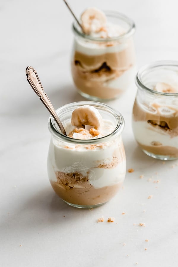 three cups of banana cream pie parfaits with graham cracker crumbs around them