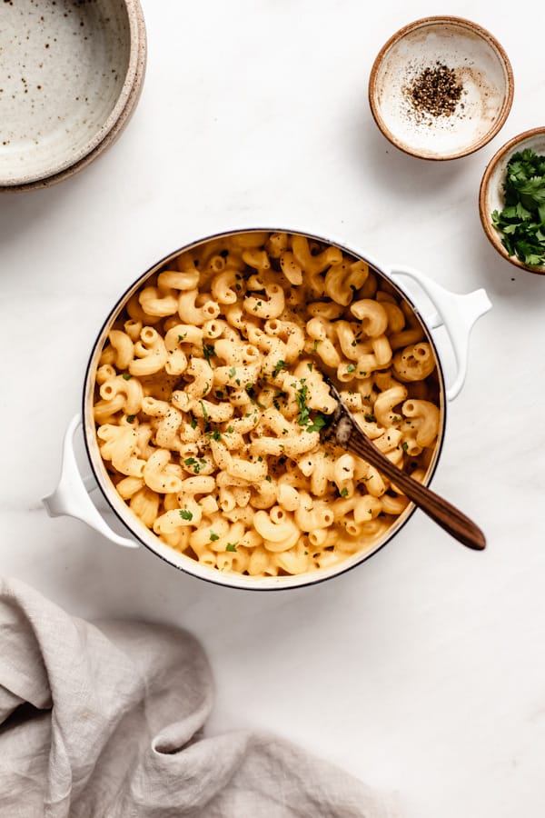 a pot of butternut squash mac and cheese with small bowls filled with parsley and pepper on the side