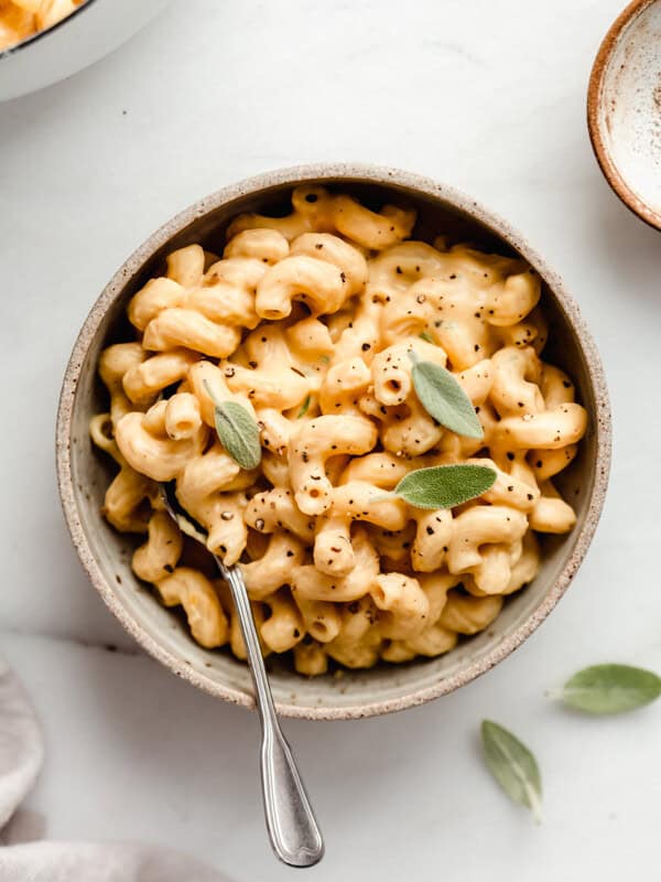 A ceramic bowl filled with butternut squash mac and cheese topped with sage leaves