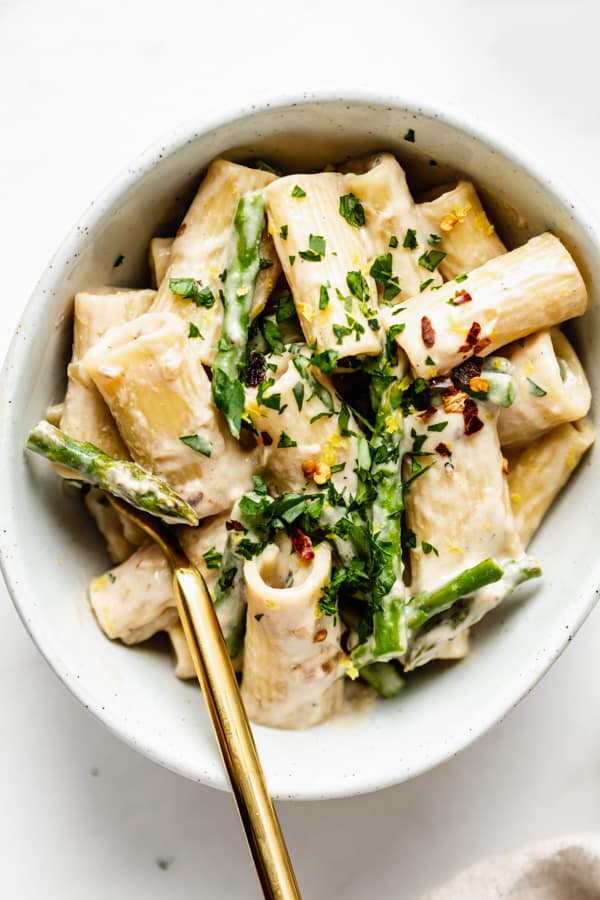 rigatoni pasta in a white bowl with a creamy white sauce, asparagus and parsely