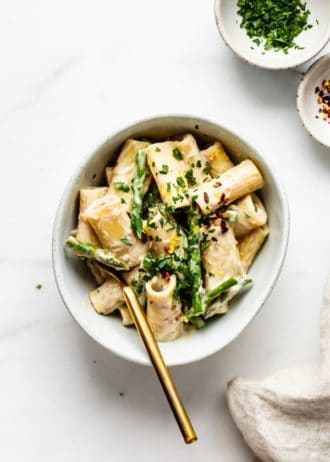 A bowl of rigatoni with asparagus and a gold fork in it