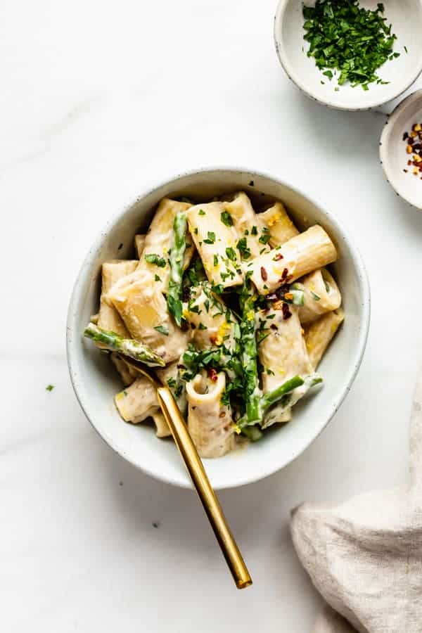 A bowl of rigatoni with asparagus and a gold fork in it