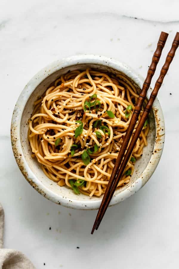 A top down view of a bowl with asian spaghetti in it topped with green onions