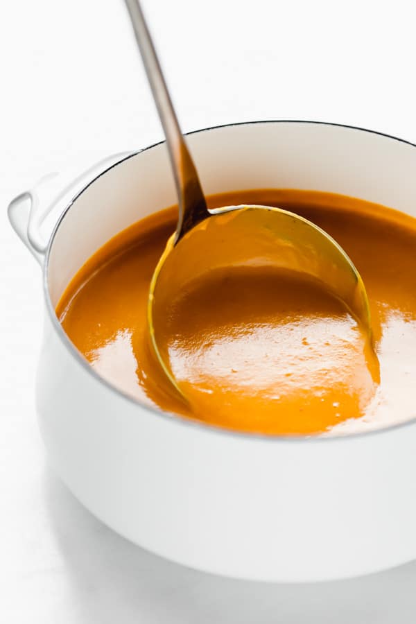 A ladle scooping out a spoonful of butternut squash soup from a pot 