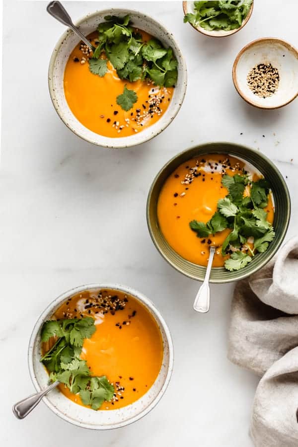 Three bowls of Thai butternut squash soup topped with cilantro on a marble counter 