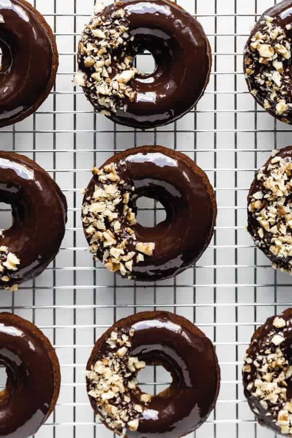 nine donuts topped with chocolate glaze on a silver cooling rack