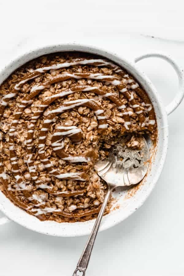 cinnamon roll baked oatmeal in a round baking dish with a serving spoon in it