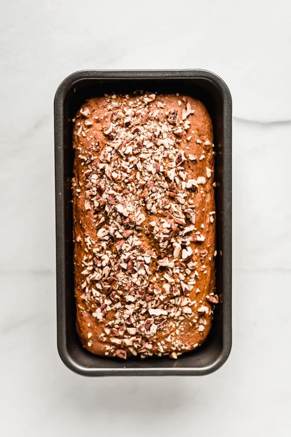 baked pumpkin bread topped with pecans in a loaf pan