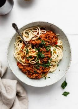 spaghetti with lentil bolognese in a white speckeld pasta bowl and a napkin on the side