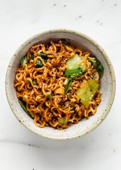 Ramen noodle stir fry in a blue ceramic bowl topped with sesame seeds