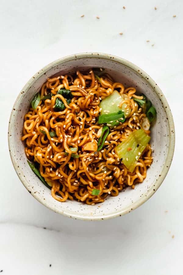 Ramen noodle stir fry in a blue ceramic bowl topped with sesame seeds