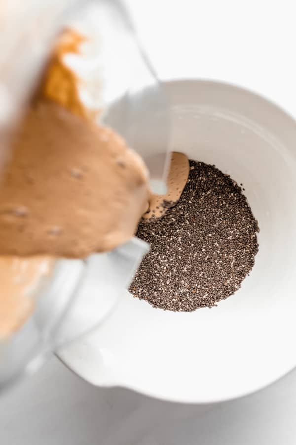 chai latte mixture being poured into a white bowl of chia seeds