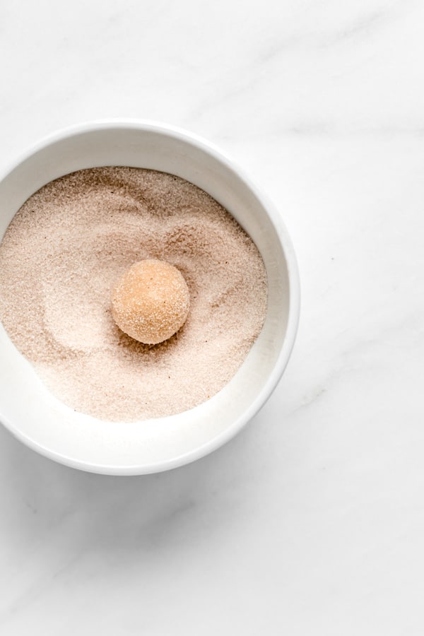 uma bola de snickerdoodle massa de biscoito em uma tigela de canela açúcar