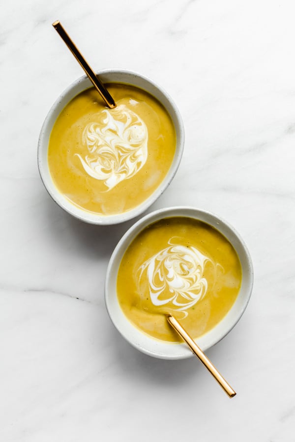 two bowl of curried coconut cauliflower soup with coconut milk swirls on them