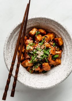 General Tso Tofu in a speckled ceramic bowl with wooden chopsticks on the side