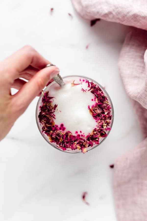 a hand mixing a spoon in a hibiscus rose latte