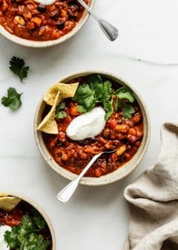 three bowls of vegan chili topped with vegan sour creme, cilantro and tortilla chips