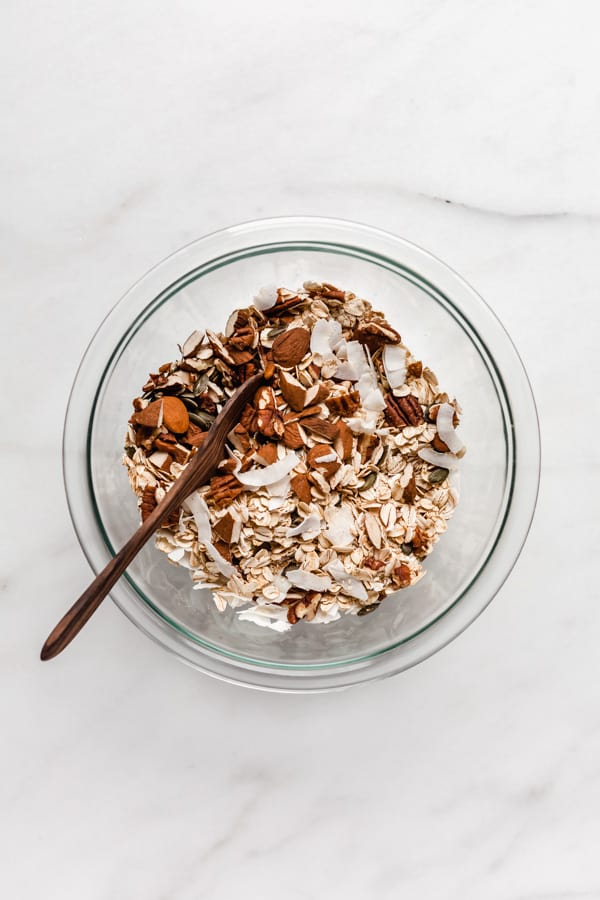 a clear mixing bowl filled with oats, coconut and nuts