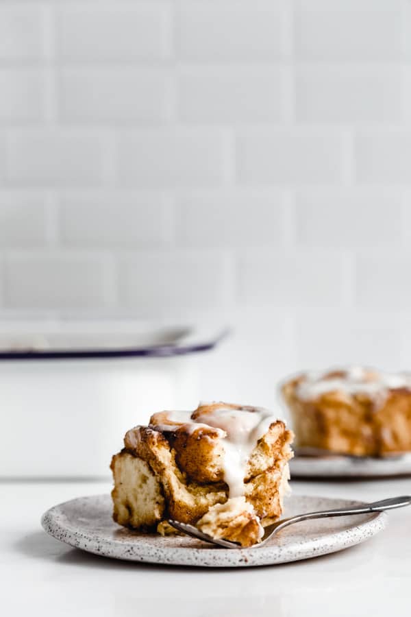 a cinnamon roll on a plate with a white pan in the background