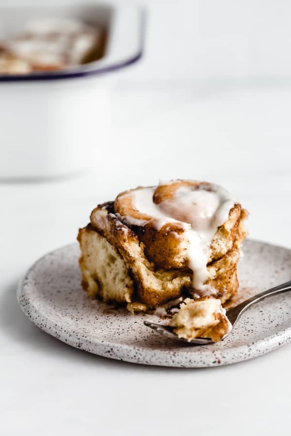 a cinnamon roll on a white plate with a fork and a bite taken out of it
