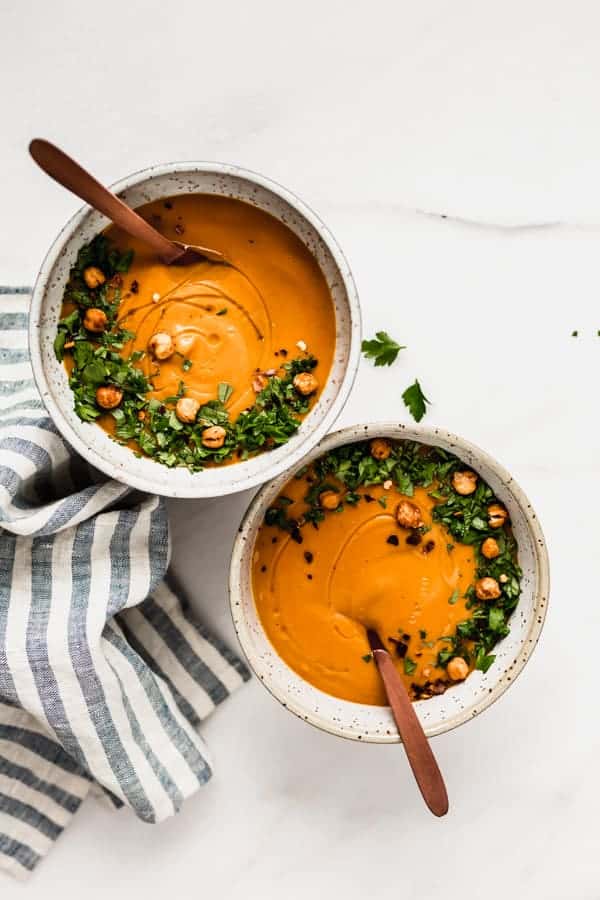 two bowls of sweet potato soup with wooden spoons in them