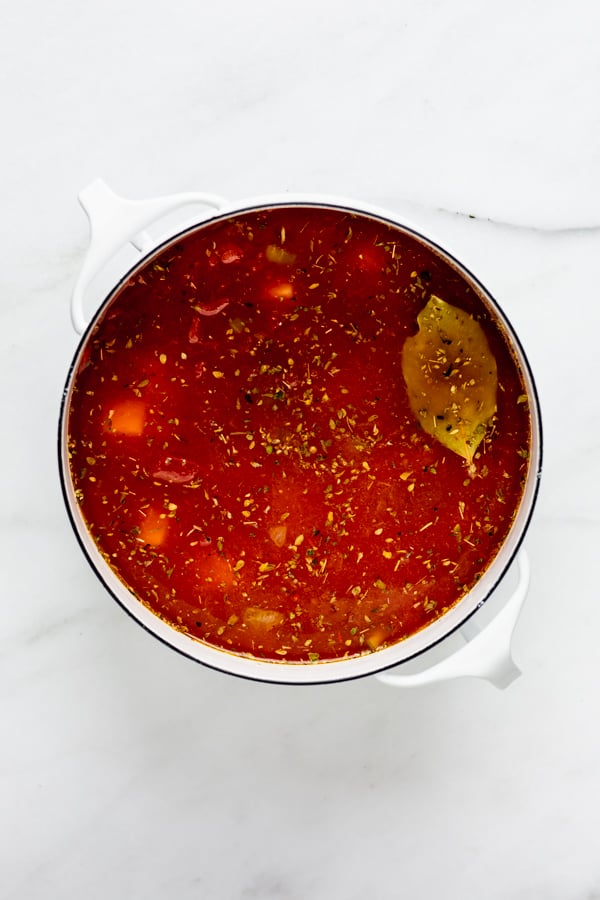 A white pot filled with vegetable broth and crushed tomatoes