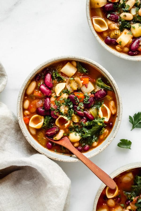 three bowls of vegan minestrone soup with a linen napkin on the side