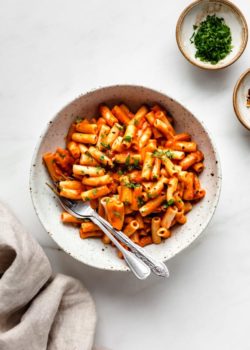 roasted red pepper pasta in a white speckled pasta bowl with a side of parsley
