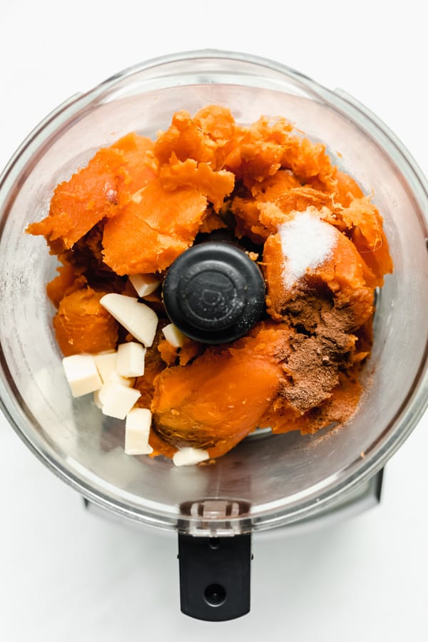 A food processor filled with sweet potatoes, salt, vegan butter and cinnamon