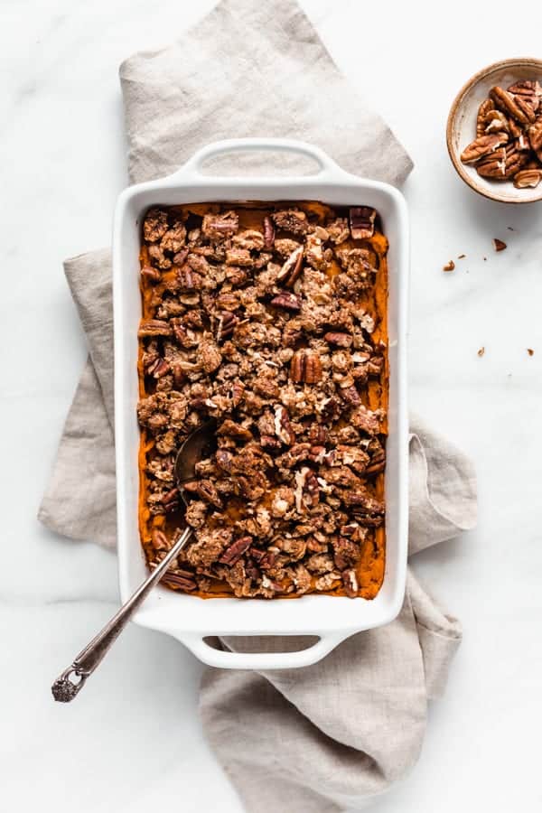 vegan sweet potato casserole in a white baking dish and a serving spoon in it