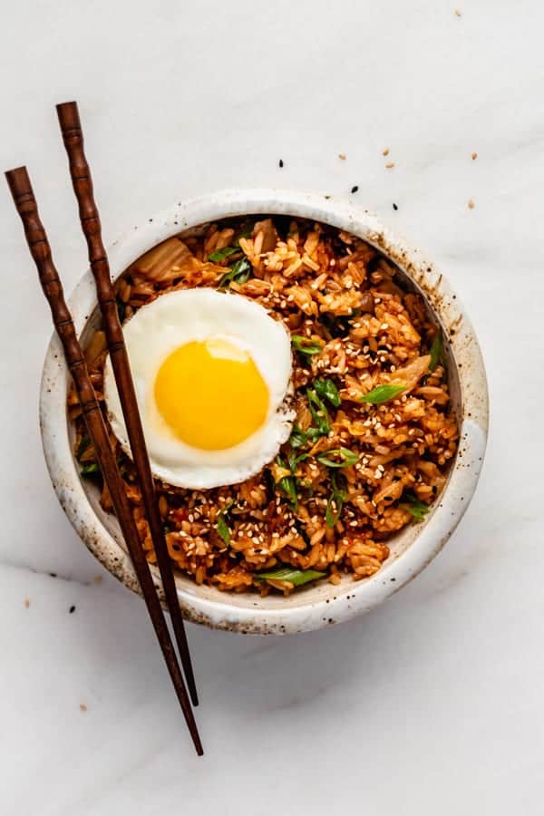 A bowl of kimchi fried rice topped with an egg and chopsticks on top