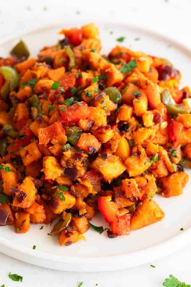 sweet potato hash topped with fresh herbs on a white plate